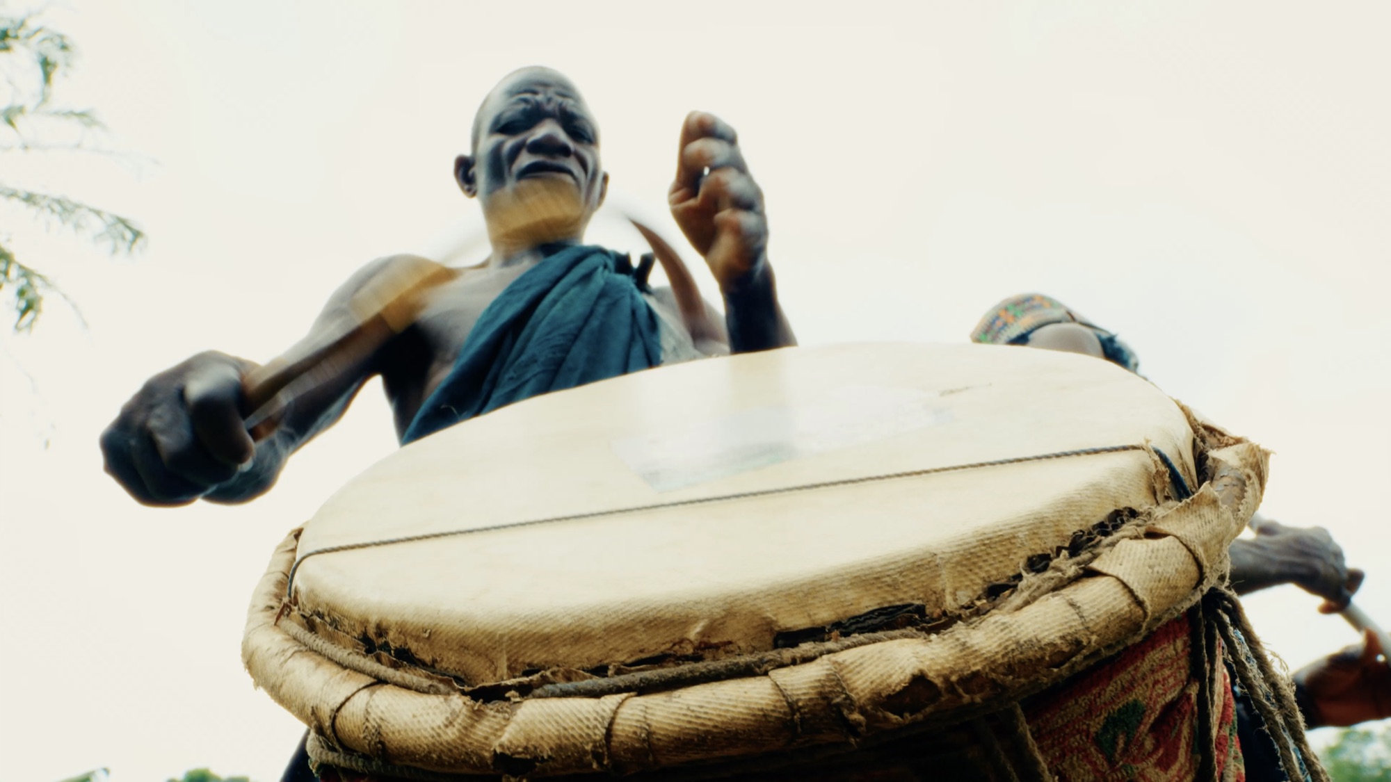 Low angle of a drummer mid-strike, framed against a pale sky
