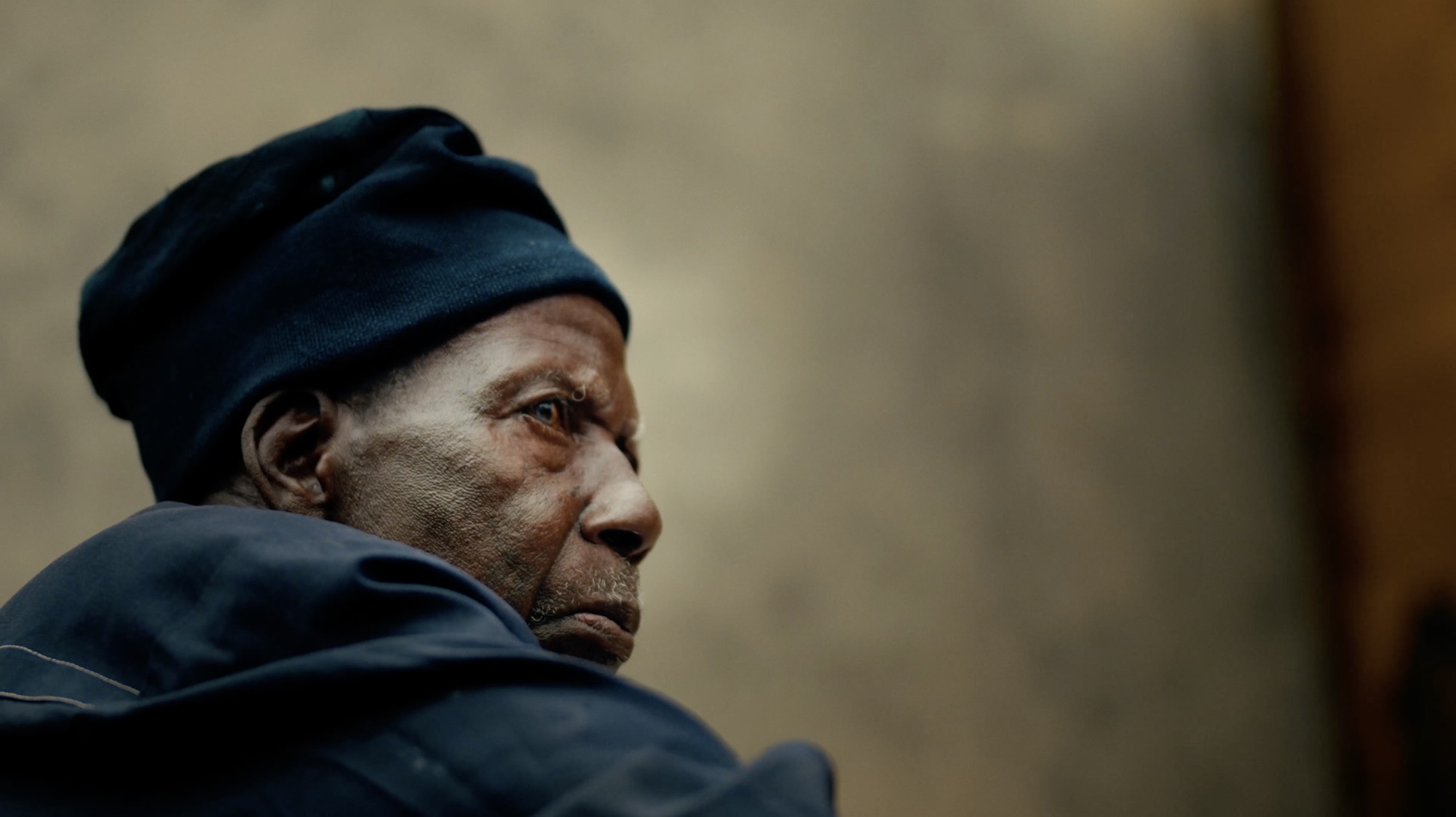 Close profile of a village elder in a dark cap against a warm ochre wall