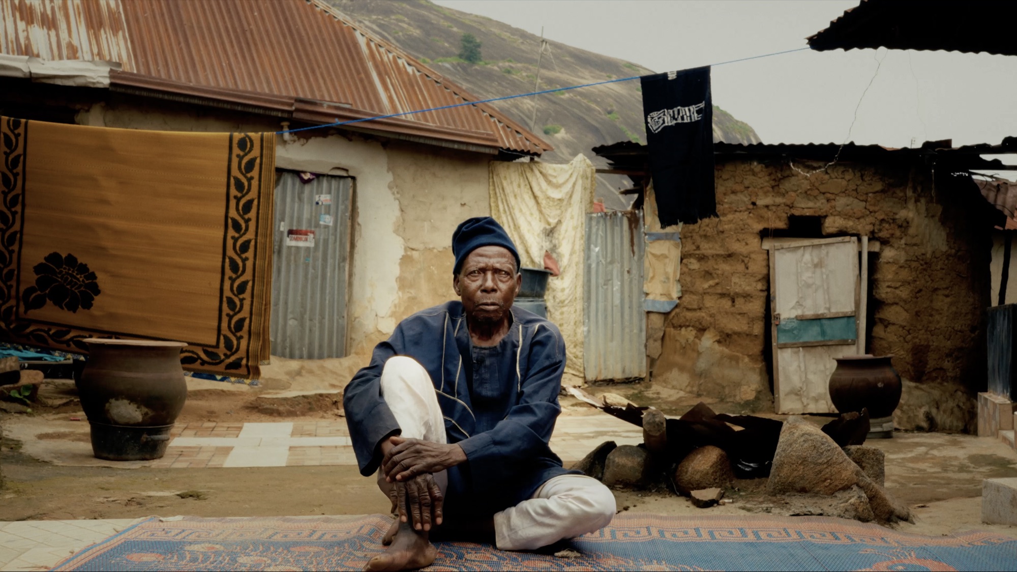 The weaver seated in his compound, finished indigo and ochre cloths hanging on lines around him