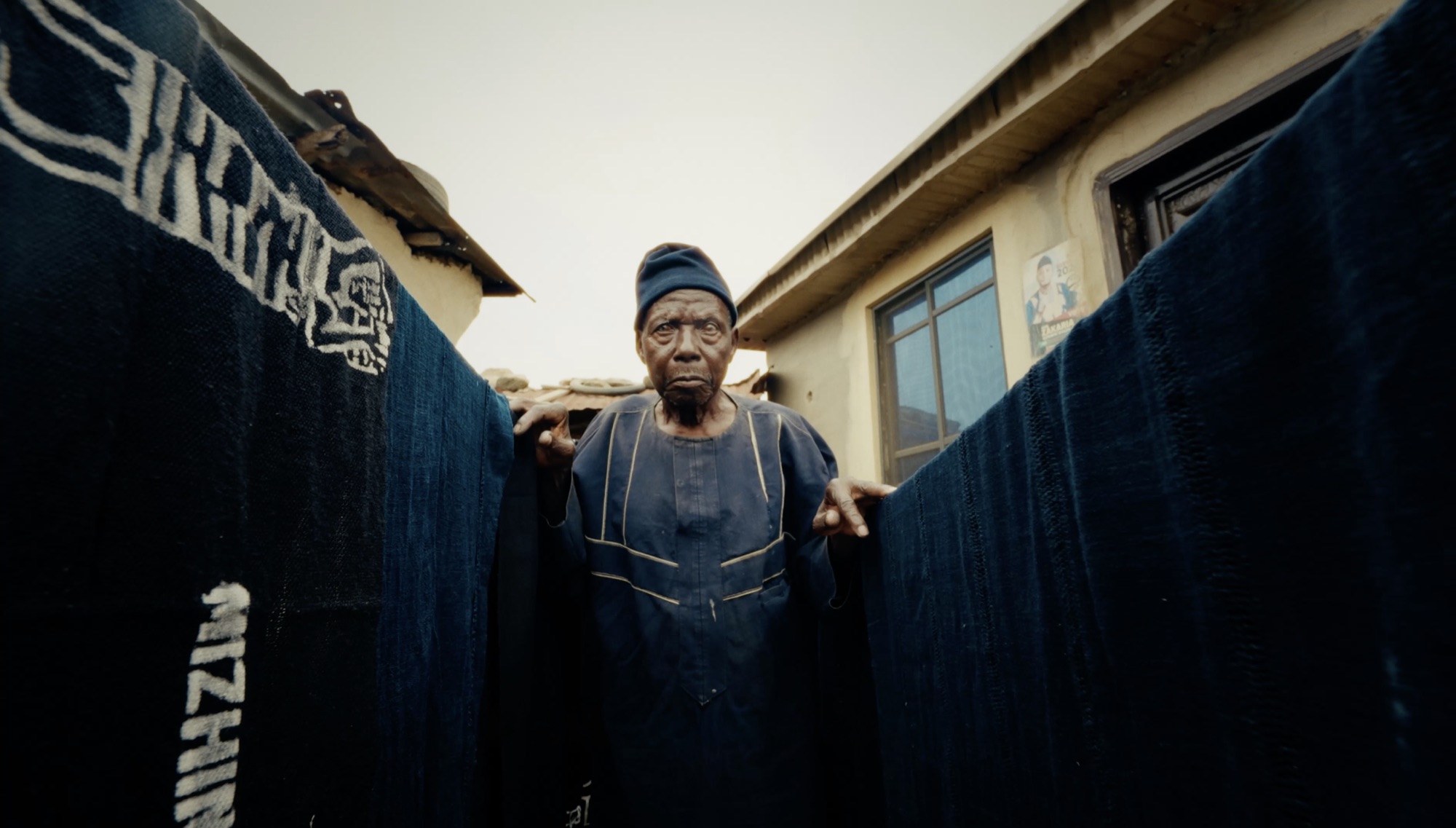 The weaver holding open two lengths of patterned indigo cloth, facing camera