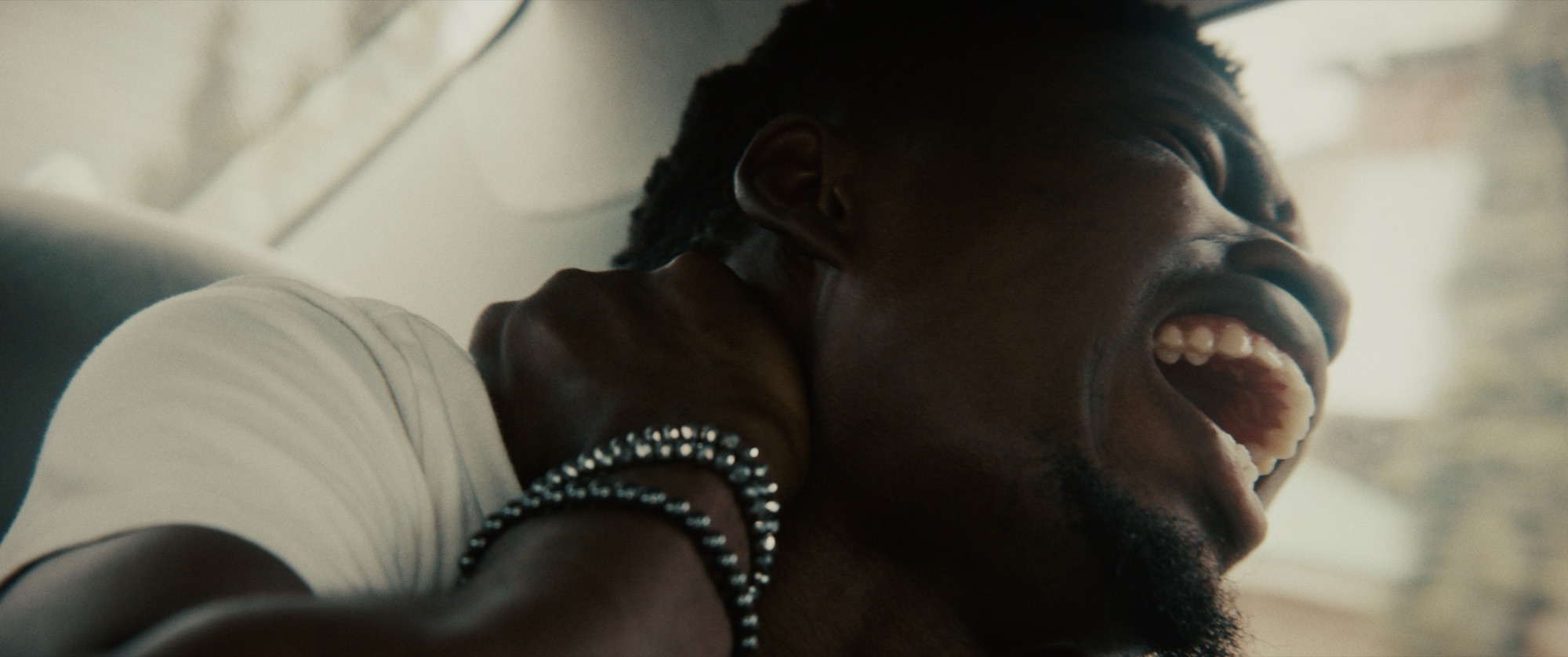 Close view of Gbenga in pain, his head tipped back and his hand gripping his shoulder