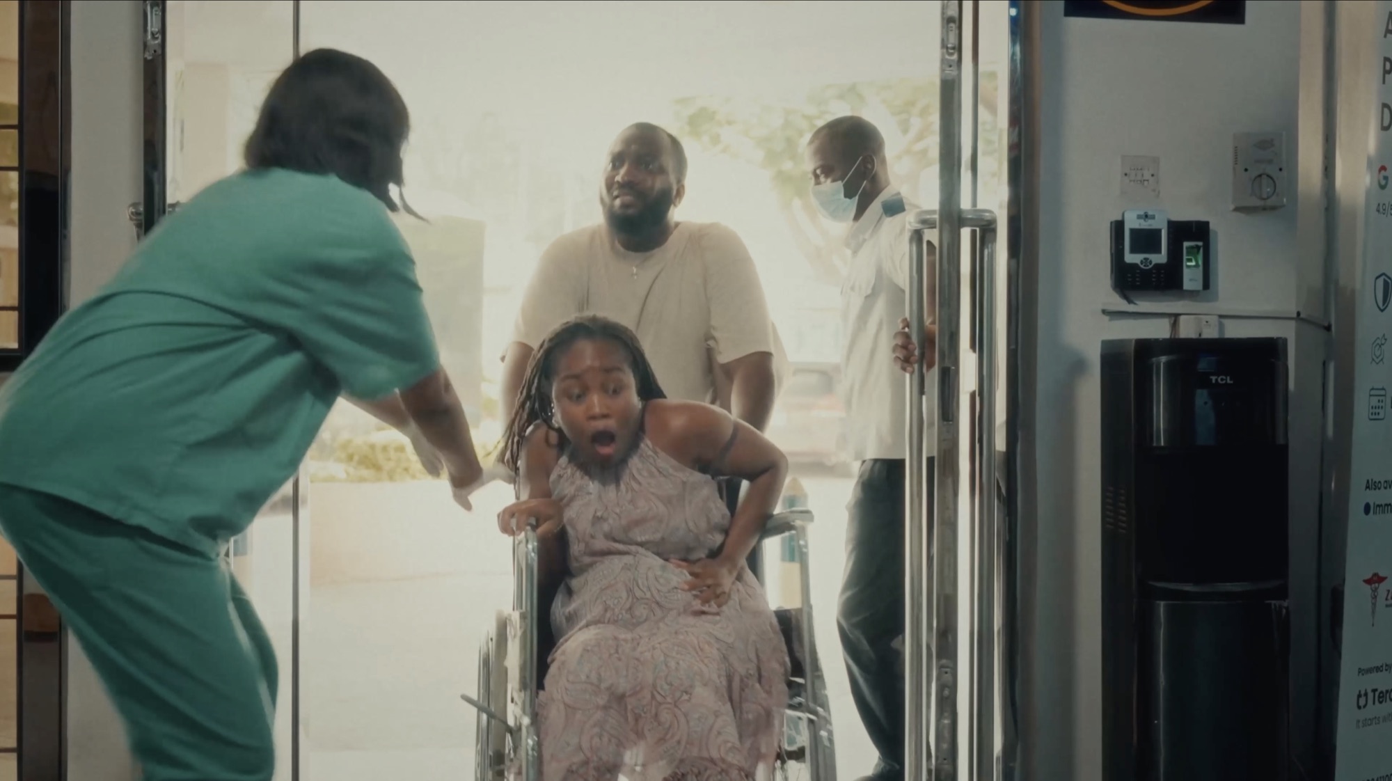 A woman in a wheelchair is rushed through hospital doors as a nurse in scrubs moves to meet her