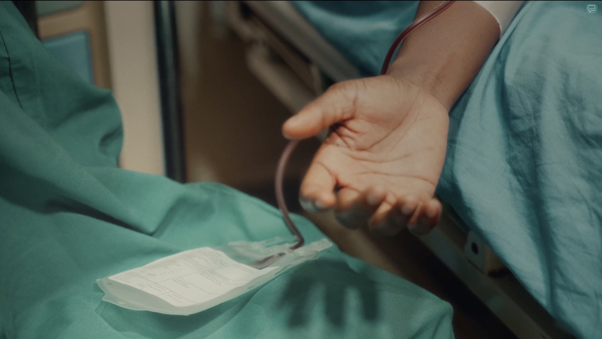 An open hand rests on a green surgical drape beside a blood bag and line